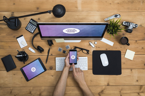 User with Desktop Computer, Tablet, and Smartphone on a Cluttered Wooden Table Mockup 2 124766571